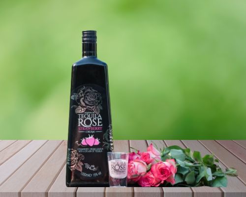 tequila rose bottle on wooden table with short glass and pink rose